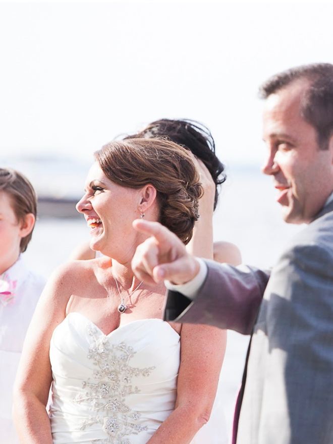 A bride laughing during her waterfront ceremony as her groom gestures to their guests