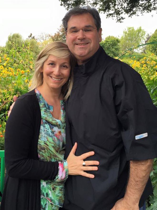Christie and her husband Charles smiling together in a sunflower garden