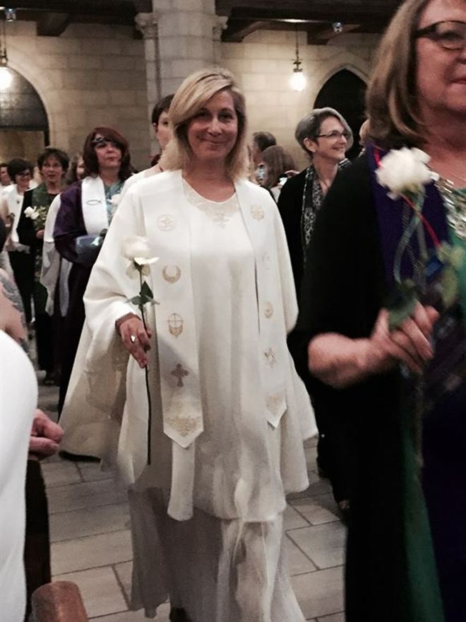 Christie in white robes carrying a white rose during her ordination procession