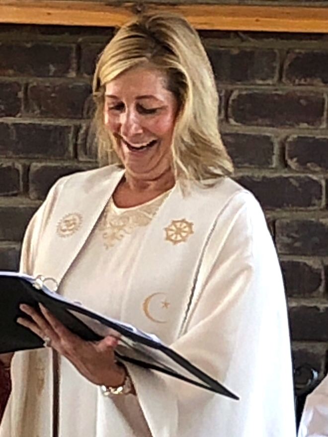Rev. Christie smiling as she reads from her ceremony book in her embroidered interfaith stole