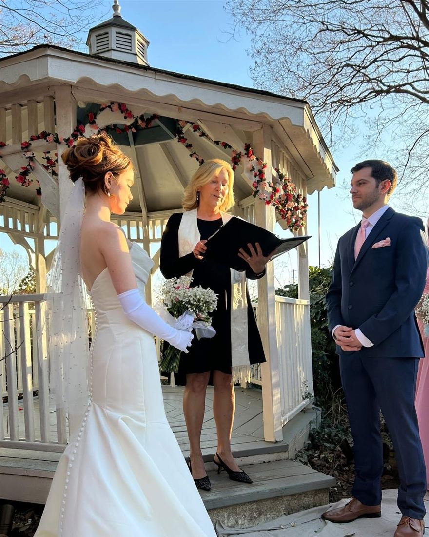Rev. Christie officiating a sunny ceremony in a white gazebo garlanded with roses