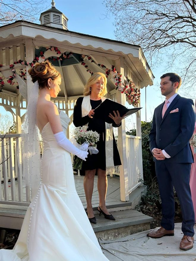 Rev. Christie reading a ceremony in a rose-garlanded gazebo as a bride and groom face each other