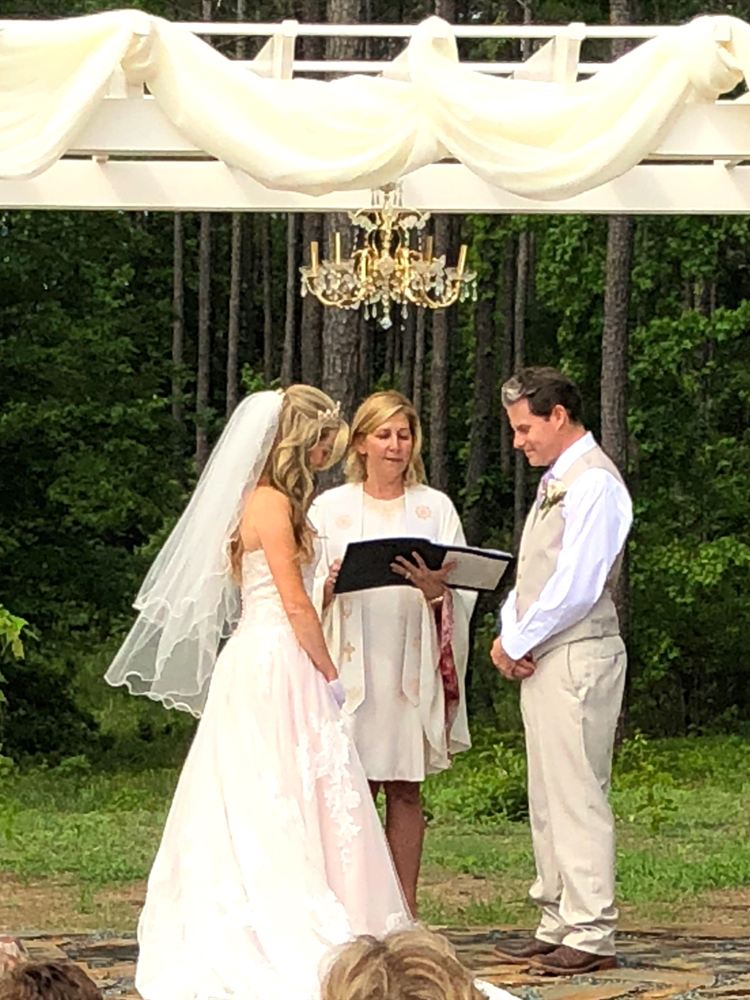 Rev. Christie officiating beneath a draped pergola with a chandelier in a pine forest