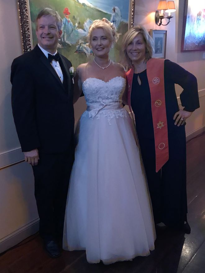 Rev. Christie with a bride and groom after their ceremony, wearing her orange stole embroidered with symbols of many faiths